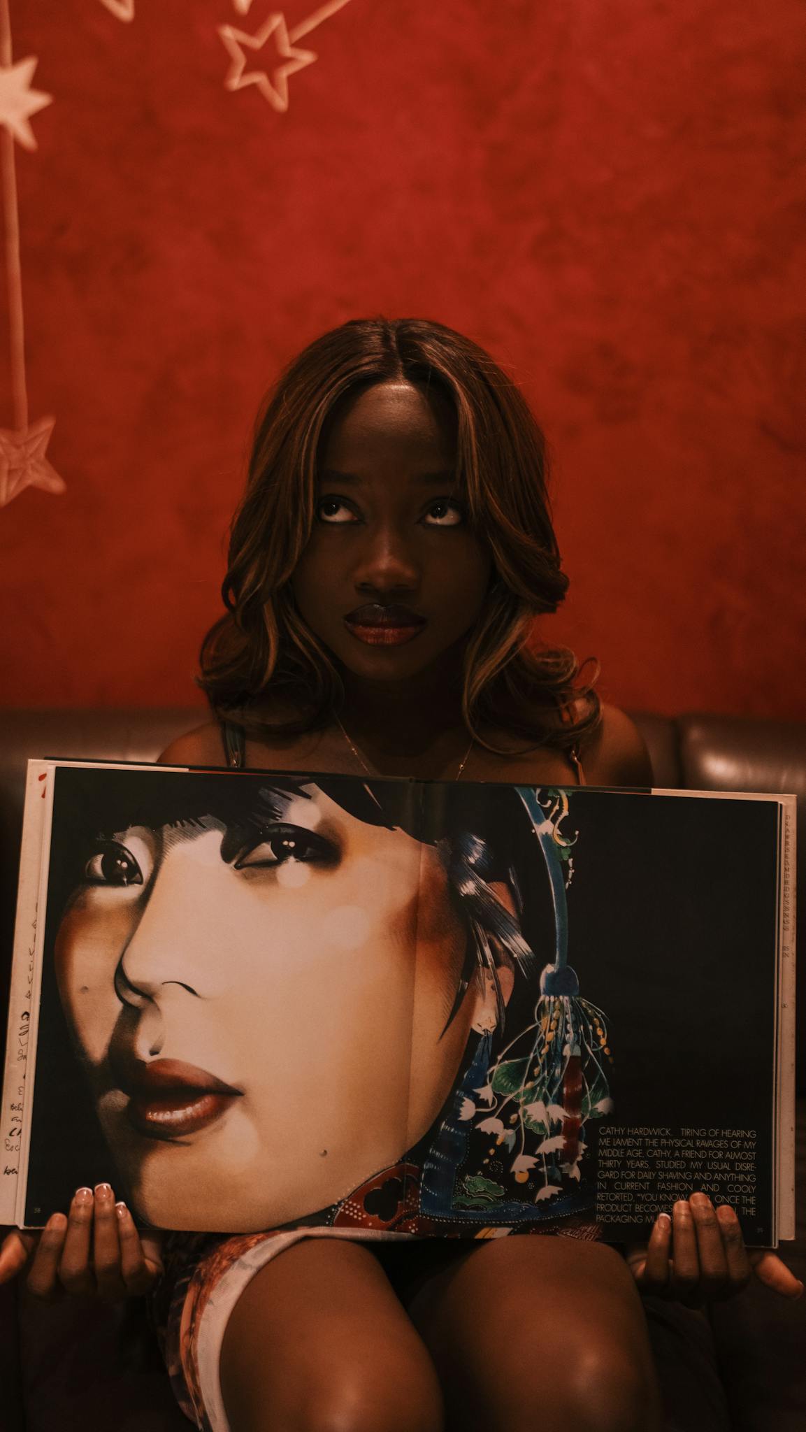 A woman holds a magazine revealing an artistic portrait against a warm, textured background.