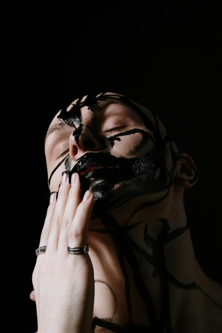Artistic portrait of a man with black face paint on a black background, highlighting expression and creativity.