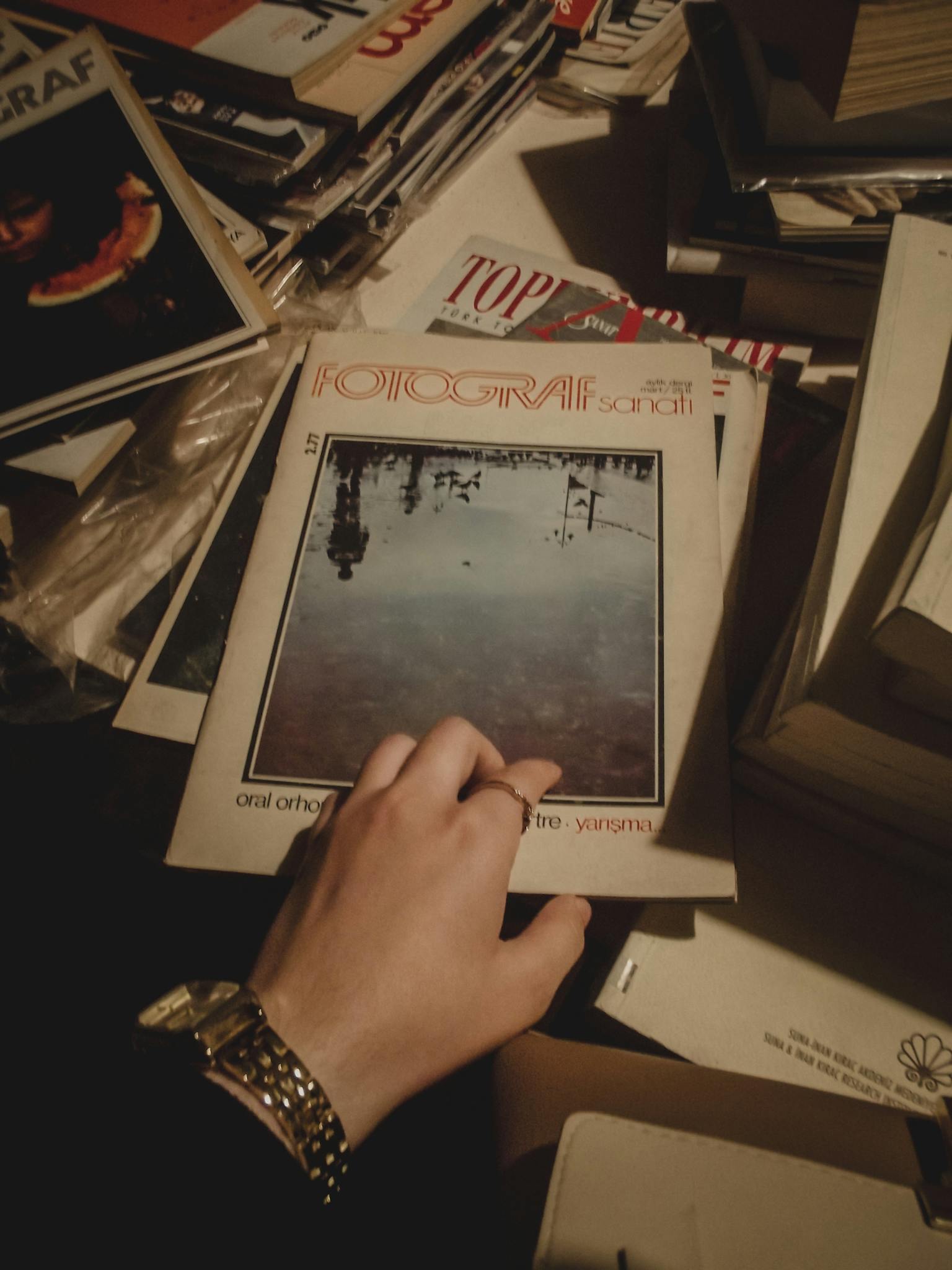 Hand picking a vintage photography magazine from a nostalgic collection stack.